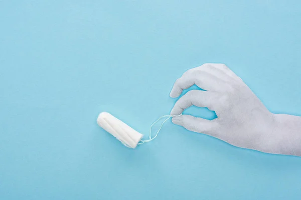 Vista superior do papel branco corte mão segurando tampão de algodão no fundo azul — Fotografia de Stock