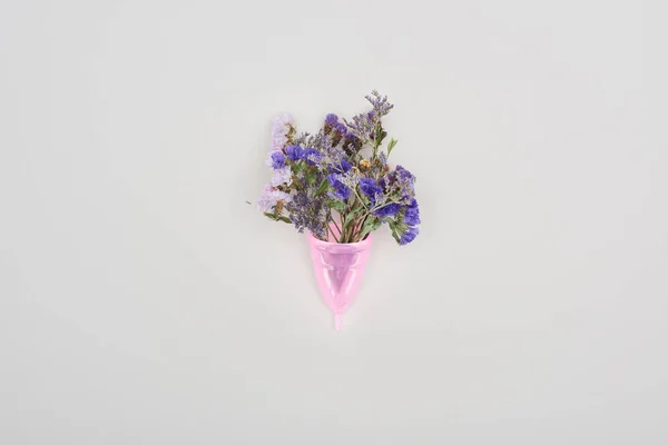 Вид зверху рожевої пластикової менструальної чашки з дикими квітами ізольовані на сірому — стокове фото