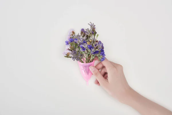 Cropped view of woman holding pink plastic menstrual cup with wildflowers isolated on grey — Stock Photo