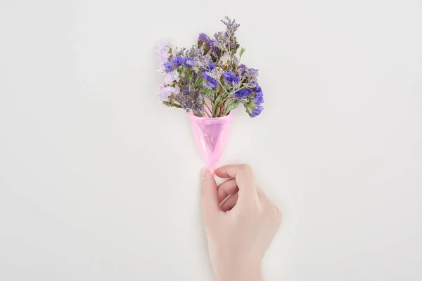 Partial view of woman holding pink plastic menstrual cup with wildflowers isolated on grey — Stock Photo