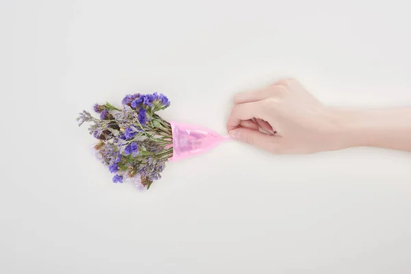 Cropped view of woman holding plastic menstrual cup with wildflowers isolated on grey — Stock Photo