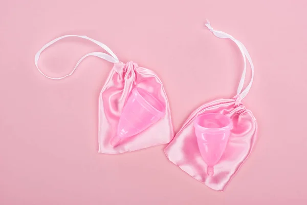 Top view of pink plastic menstrual cups in bags on pink background — Stock Photo