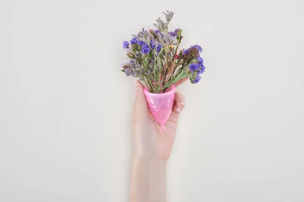 Cropped view of woman holding pink menstrual cup with wildflowers isolated on grey — Stock Photo