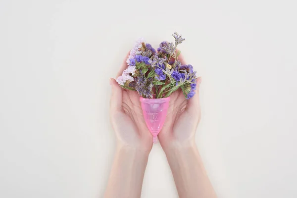 Vista cortada de mulher segurando copo menstrual com flores silvestres isoladas em cinza — Fotografia de Stock