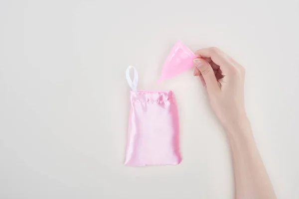 Cropped view of woman holding pink plastic menstrual cup near bag isolated on grey — Stock Photo