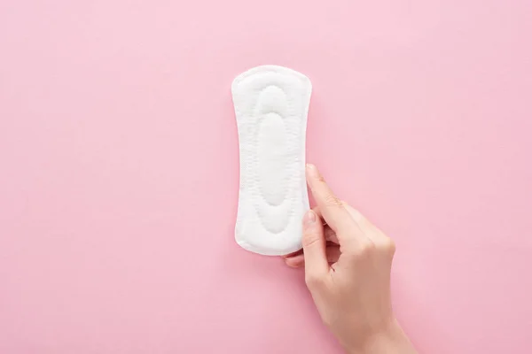 Cropped view of woman holding white sanitary napkin on pink background — Stock Photo