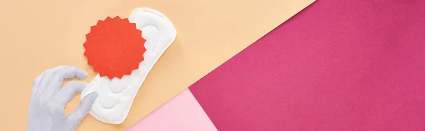 Colpo panoramico di mano bianca con tovagliolo sanitario e cartellino rosso su sfondo rosa, viola e beige — Foto stock