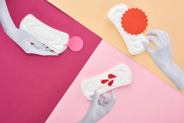 Vista superior del papel cortado manos blancas con toallas sanitarias blancas cerca de tarjetas vacías y gotas de sangre sobre fondo púrpura, rosa y beige - foto de stock