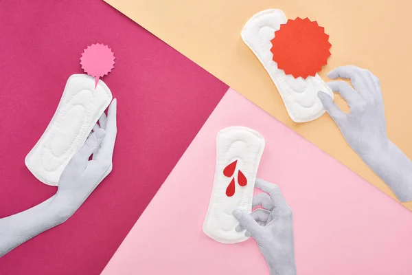 Vista dall'alto di mani tagliate di carta con assorbenti igienici bianchi vicino a carte vuote e gocce di sangue su sfondo viola, rosa e beige — Foto stock