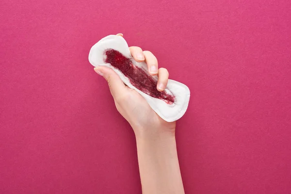 Partial view of woman holding sanitary towel with blood on purple background — Stock Photo