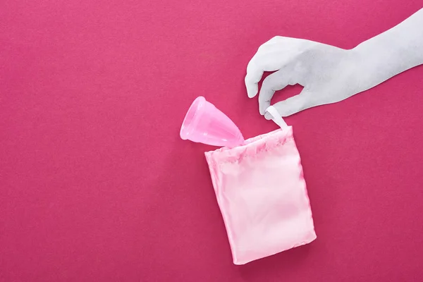 Vista dall'alto di carta tagliata mano bianca con tazza mestruale di plastica in borsa su sfondo viola — Foto stock