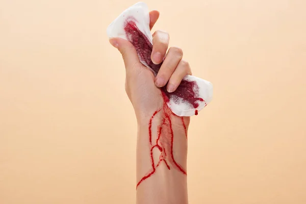 Частковий вид жінки стискає санітарний рушник з кров'ю ізольовано на бежевому — стокове фото