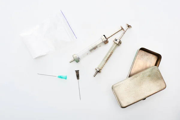 Top view of aged syringes with needles near heroin and metal box on white background — Stock Photo