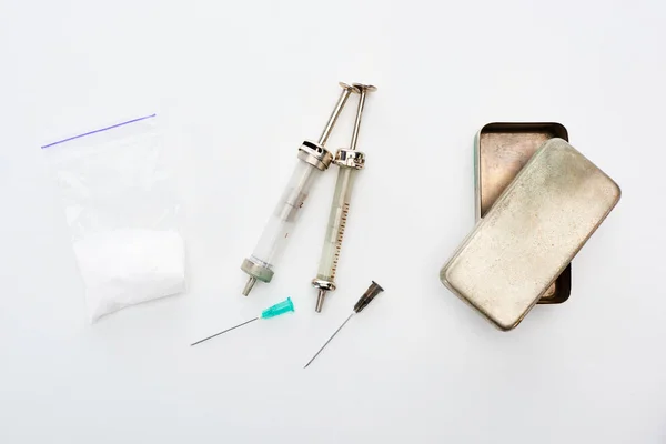 Vue du dessus des seringues avec aiguilles près de l'héroïne et de la boîte métallique sur fond blanc — Photo de stock