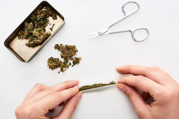 Cropped view of woman rolling joint near marijuana buds in box and scissors — Stock Photo