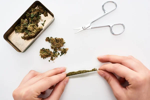 Vue recadrée de femme roulant joint près de bourgeons de marijuana dans la boîte et ciseaux — Photo de stock