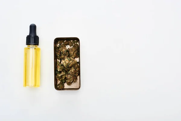 Piatta giaceva con cannabis in contenitore di metallo vicino cbd olio in bottiglia su sfondo bianco — Foto stock