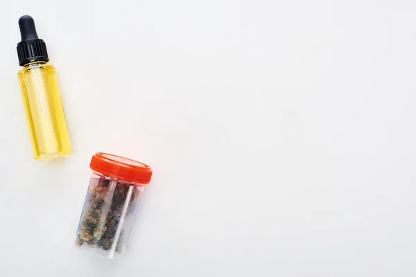 Vista superior de cannabis em recipiente de plástico perto de óleo de cbd em garrafa no fundo branco — Fotografia de Stock