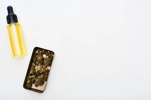 Vista superior de cannabis em recipiente de metal perto de óleo de cbd em garrafa no fundo branco — Fotografia de Stock