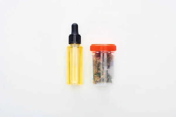 Flat lay com cannabis em recipiente de plástico perto de óleo de cbd em garrafa no fundo branco — Fotografia de Stock