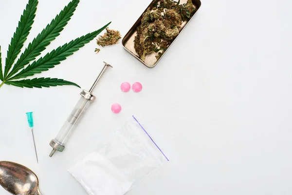 Top view of marijuana buds, cannabis leaf, spoon, heroin, lsd and syringe on white background — Stock Photo