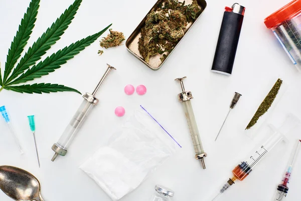 Vista superior de brotes de marihuana, hoja de cannabis, heroína, pastillas y jeringas sobre fondo blanco - foto de stock