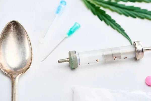 Vue rapprochée de la feuille de cannabis, cuillère argentée, seringue, aiguilles, héroïne et lsd — Photo de stock