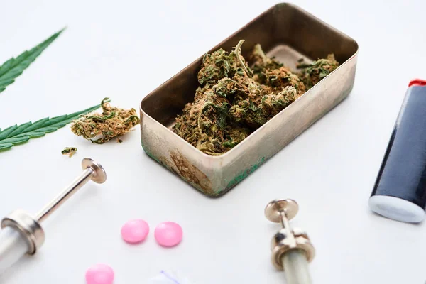 Vue rapprochée des bourgeons de marijuana, seringues et briquet près de l'ecstasy rose sur fond blanc — Photo de stock