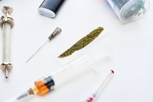 Selective focus of syringes near rolling paper with marijuana on white background — Stock Photo