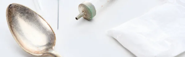 Cuchara de plata, jeringa, aguja y heroína sobre fondo blanco, tiro panorámico - foto de stock
