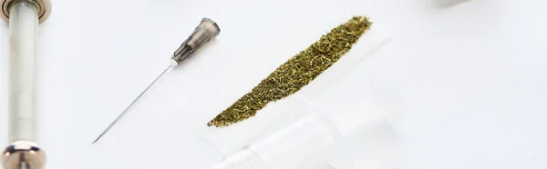 Selective focus of syringes near rolling paper with marijuana on white background, panoramic shot — Stock Photo
