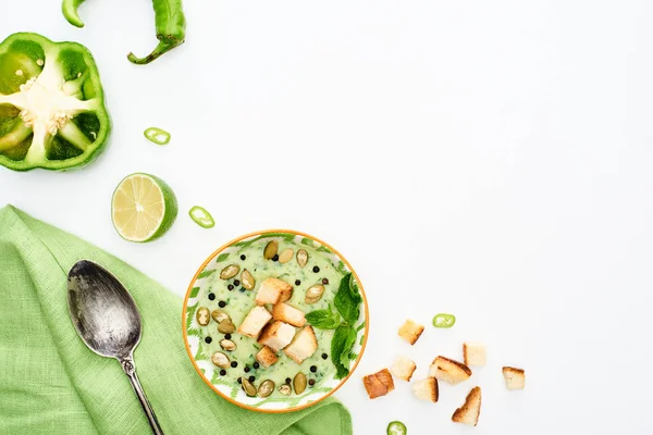 Top view of delicious creamy green vegetable soup with croutons served with napkin and spoon isolated on white — Stock Photo