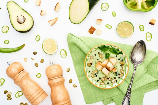Вид на вкусный сливочно-зеленый овощной суп рядом с перцово-солевыми мельницами и разбросанными ингредиентами, изолированными на белом — стоковое фото
