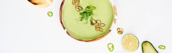 Panoramic shot of delicious creamy green vegetable soup near lime and jalapenos isolated on white — Stock Photo