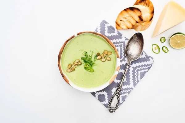 Vue du dessus de délicieuse soupe de légumes vert crémeux servi sur serviette près de cuillère avec croûtons grillés et fromage isolé sur blanc — Photo de stock