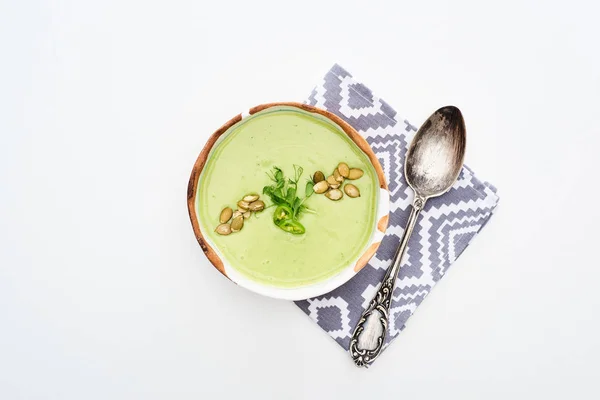 Vista superior de deliciosa sopa de legumes verde cremoso com brotos e sementes de abóbora em guardanapo com colher isolada em branco — Fotografia de Stock