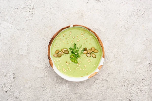 Top view of tasty green creamy soup with pumpkin seeds on textured grey background with rustic cloth — Stock Photo