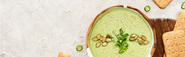 Vista dall'alto di gustosa zuppa verde cremosa con cracker su tagliere di legno, colpo panoramico — Foto stock