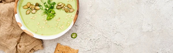 Draufsicht auf leckere grüne cremige Suppe mit Crackern auf strukturiertem grauen Hintergrund mit rustikalem Tuch, Panoramaaufnahme — Stockfoto