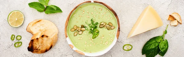 Панорамный снимок вкусного зеленого сливочного супа с гренками, сыром и шпинатом на сером фоне с текстурой — стоковое фото