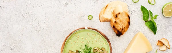 Panoramische Aufnahme einer leckeren grünen cremigen Suppe mit Croutons und Käse auf strukturiertem grauen Hintergrund — Stockfoto