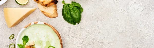 Panoramic shot of tasty green creamy soup with croutons and cheese on textured grey background — Stock Photo