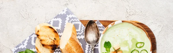 Панорамный снимок зеленого овощного сливочного супа на деревянной доске с салфеткой, ложкой и гренками — стоковое фото