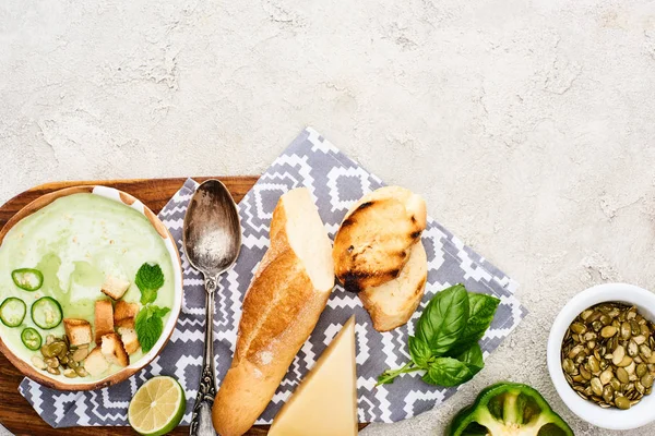 Vista dall'alto della zuppa di verdure verdi cremose sul tagliere di legno con tovagliolo e ingredienti vicino ai semi di zucca — Foto stock