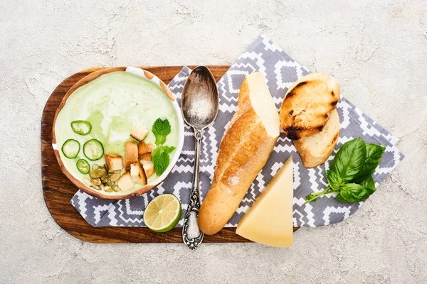Top view of green vegetable creamy soup on wooden chopping board with napkin, spoon and ingredients — Stock Photo