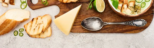 Panoramic shot of green vegetable creamy soup on wooden chopping board on textured surface — Stock Photo