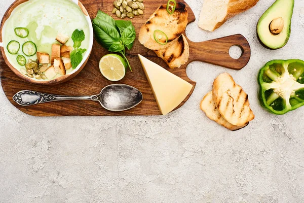 Top view of green vegetable creamy soup on wooden chopping board on textured surface — Stock Photo