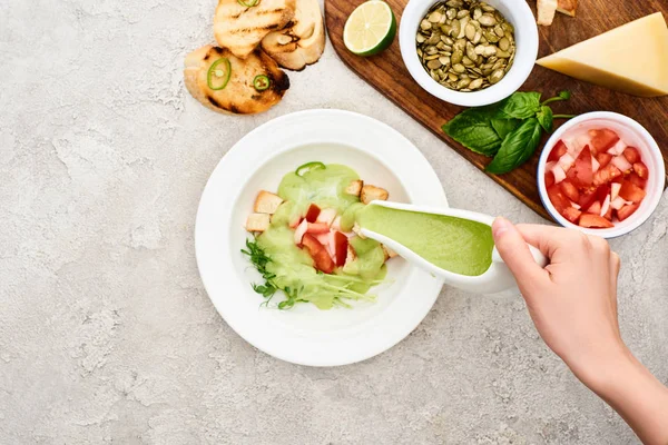 Partial view of woman cooking green creamy soup near wooden cutting board with fresh ingredients — Stock Photo