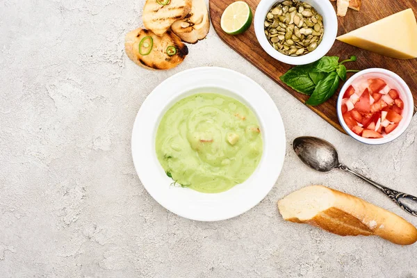Top view of green creamy soup near spoon and wooden cutting board with fresh ingredients — Stock Photo