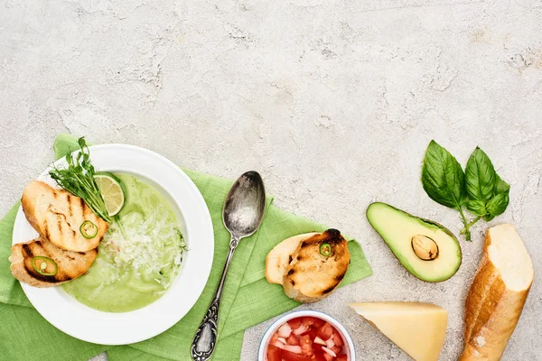 Vista dall'alto di deliziosa zuppa di verdure verdi cremose con crostini serviti con cucchiaio su tovagliolo vicino a ingredienti freschi — Foto stock